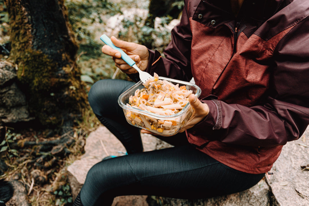 person-sits-on-a-rock-outdoors-and-eats-pasta-salad - Ready Sweat Go